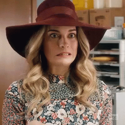 A Woman Wearing A Hat And A Floral Dress Is Making A Face . GIF