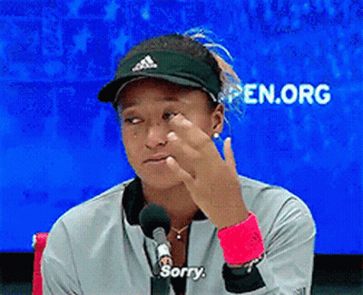 A Woman Wearing A Hat And A Jacket Says Sorry In Front Of A Microphone GIF