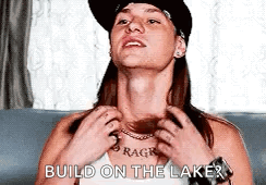 A Woman Wearing A Hat And A Necklace Is Sitting On A Couch . GIF