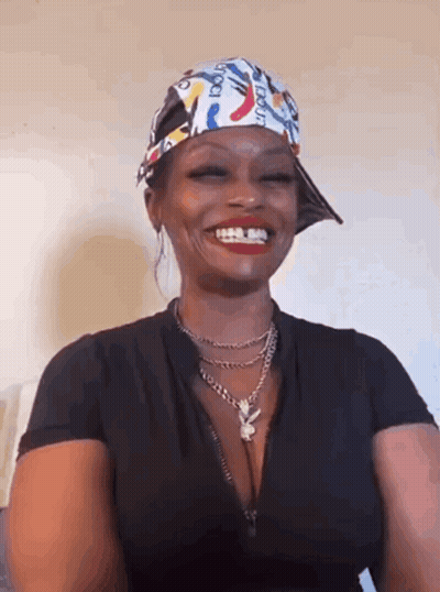 A Woman Wearing A Hat And A Necklace Is Smiling And Wearing A Bandana . GIF