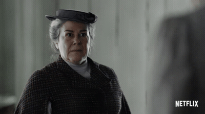 A Woman Wearing A Hat And A Plaid Coat With A Netflix Logo In The Corner GIF