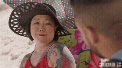 A Woman Wearing A Hat And A Red Bikini Is Sitting On A Beach Chair Looking At A Man . GIF