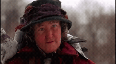 A Woman Wearing A Hat And A Red Coat Is Standing In The Snow GIF
