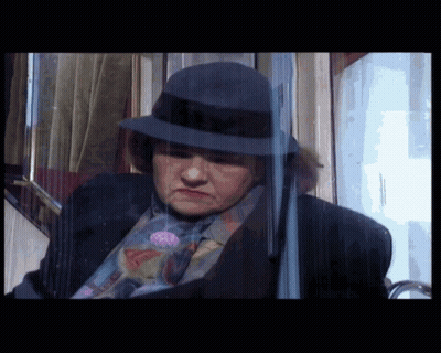 A Woman Wearing A Hat And A Suit Is Behind A Glass GIF