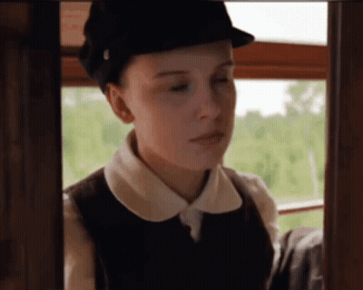 A Woman Wearing A Hat And A Vest Looks Out A Window . GIF