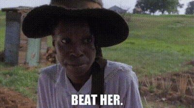 A Woman Wearing A Hat And A White Shirt Is Standing In A Field With The Words `` Beat Her '' . GIF