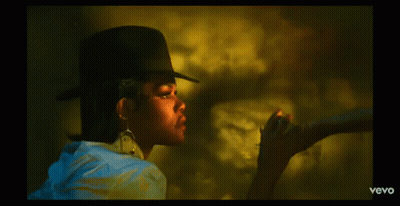 A Woman Wearing A Hat And Earrings Is Smoking A Cigarette In A Vevo Video GIF