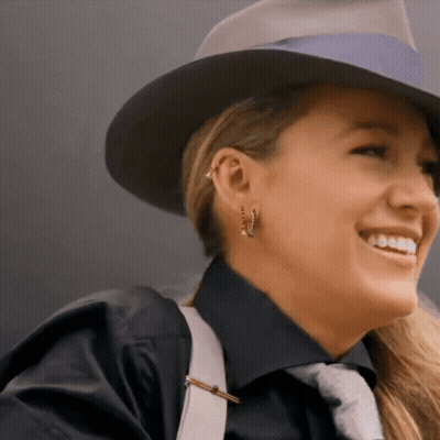 A Woman Wearing A Hat And Earrings Smiles For The Camera GIF