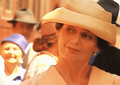 A Woman Wearing A Hat And Earrings Stands In A Crowd Of People GIF