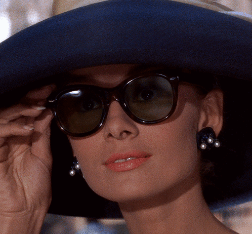 A Woman Wearing A Hat And Sunglasses Adjusts Her Glasses GIF