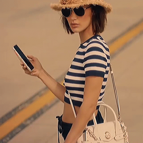 A Woman Wearing A Hat And Sunglasses Is Carrying A White Michael Kors Purse GIF