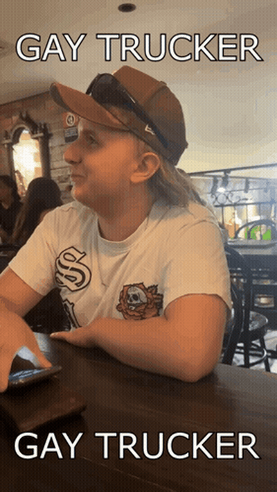A Woman Wearing A Hat And Sunglasses Is Sitting At A Table With The Caption Gay Trucker Gay Trucker GIF