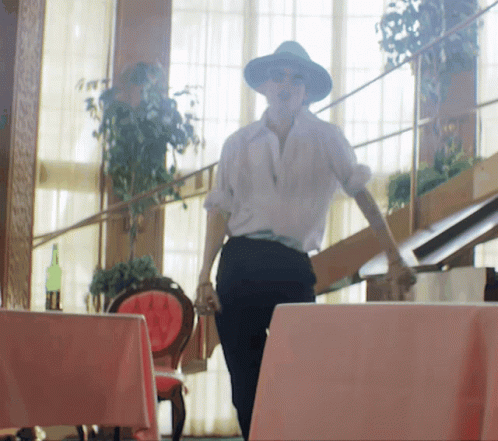 A Woman Wearing A Hat And Sunglasses Is Walking Down Stairs GIF