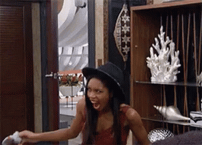 A Woman Wearing A Hat Is Sitting In A Room With A Shelf Full Of Seashells . GIF