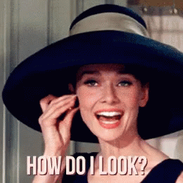 A Woman Wearing A Hat Is Smiling And Asking How Do I Look ? GIF