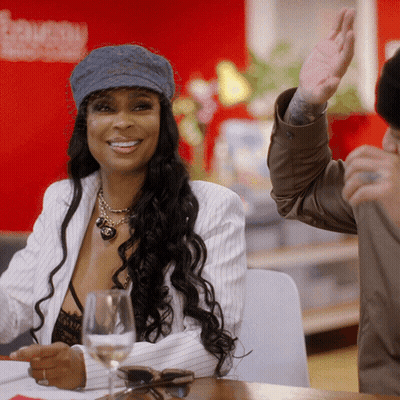 A Woman Wearing A Hat Is Smiling While Sitting At A Table GIF