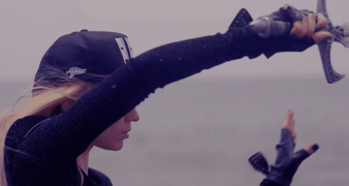 A Woman Wearing A Hat With The Letter T On It Is Holding A Sword GIF