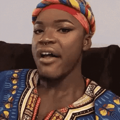 A Woman Wearing A Head Scarf And A Colorful Shirt Is Sitting In A Chair . GIF