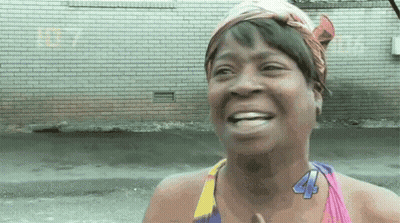 A Woman Wearing A Head Scarf And A Necklace With The Number 44 On It Is Smiling . GIF