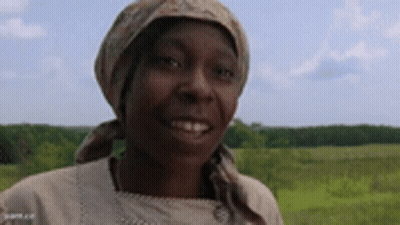 A Woman Wearing A Head Scarf And A Scarf Around Her Head Is Smiling In A Field . GIF