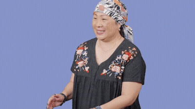 A Woman Wearing A Head Scarf Is Standing In Front Of A Sign That Says Oops GIF