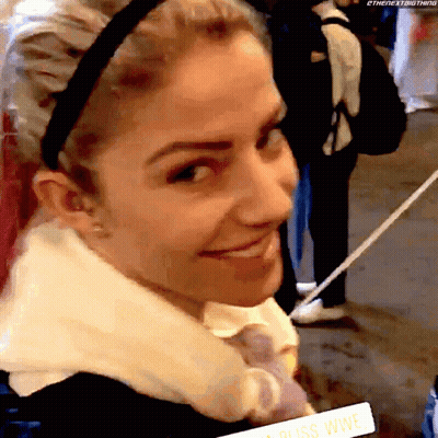 A Woman Wearing A Headband Is Smiling And Holding A Sign That Says ' Bliss Wwe ' On It GIF