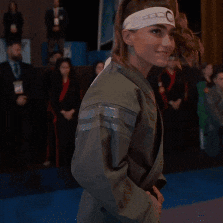 A Woman Wearing A Headband With The Letter G On It Is Covering Her Mouth With Her Hand . GIF