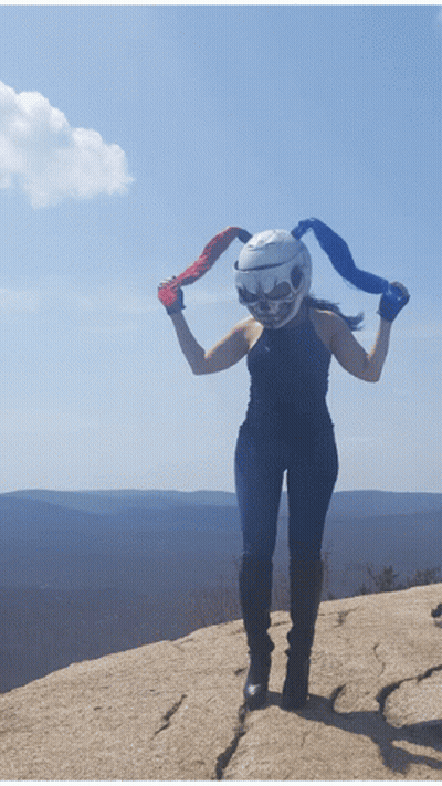 A Woman Wearing A Helmet With A Skull On It Stands On A Rock GIF