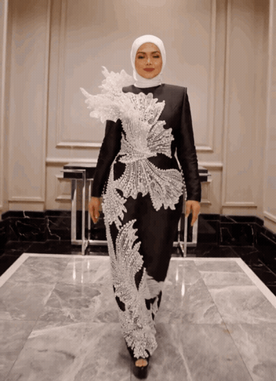 A Woman Wearing A Hijab And A Black And White Dress Is Standing In A Hallway GIF