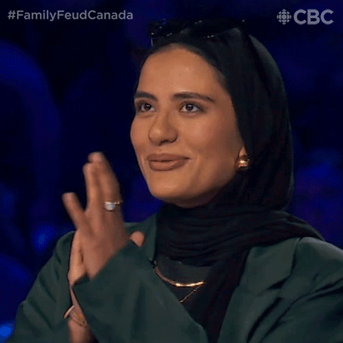 A Woman Wearing A Hijab Is Clapping Her Hands While Smiling . GIF
