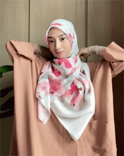 A Woman Wearing A Hijab Is Holding A Pink And White Scarf Around Her Neck GIF