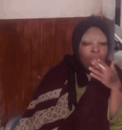 A Woman Wearing A Hijab Is Smoking A Cigarette While Sitting On A Chair . GIF