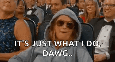 A Woman Wearing A Hoodie And Sunglasses Is Sitting In A Crowd Of People And Making A Funny Face . GIF