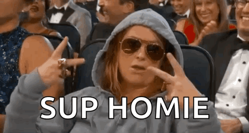 A Woman Wearing A Hoodie And Sunglasses Is Sitting In A Crowd Of People And Making A Funny Face . GIF
