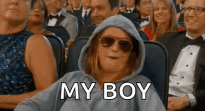 A Woman Wearing A Hoodie And Sunglasses Is Sitting In A Crowd Of People And Says `` My Boy '' . GIF