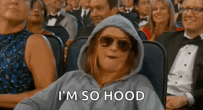 A Woman Wearing A Hoodie And Sunglasses Is Sitting In A Crowd Of People At An Event . GIF