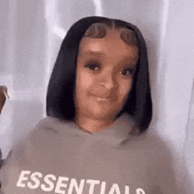 A Woman Wearing A Hoodie With The Word Essentials On It Is Looking At The Camera . GIF
