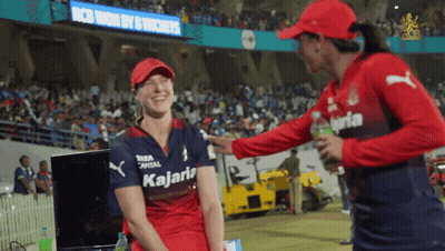 A Woman Wearing A Kalaria Shirt Talks To Another Woman In A Red Hat GIF