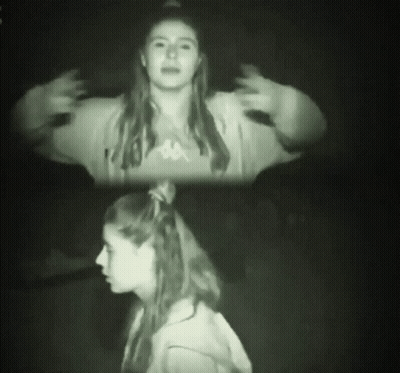 A Woman Wearing A Kappa Sweatshirt Stands In The Dark GIF