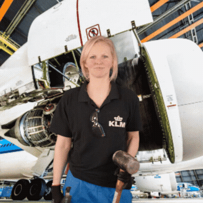 A Woman Wearing A Klm Shirt Holds A Hammer In Front Of An Airplane GIF