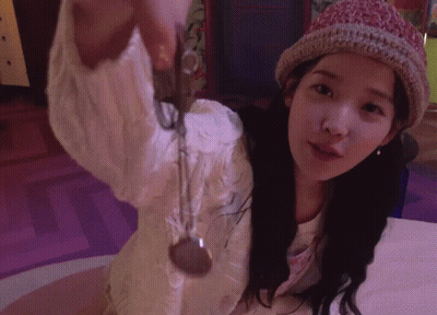 A Woman Wearing A Knitted Hat Holds A Necklace In Her Hand GIF