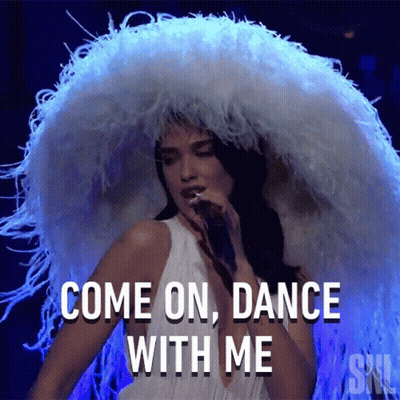 A Woman Wearing A Large White Feathered Hat Is Singing Into A Microphone And Says Come On Dance With Me GIF