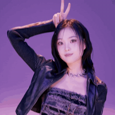 A Woman Wearing A Leather Jacket And A Necklace Is Making A Peace Sign GIF