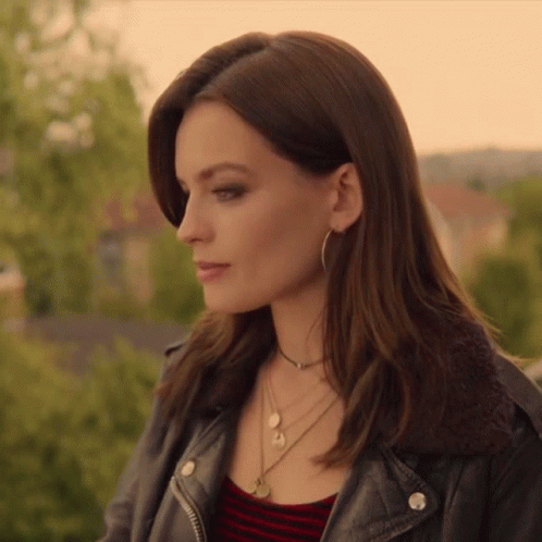 A Woman Wearing A Leather Jacket And A Necklace Looks To The Side GIF