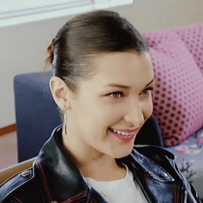 A Woman Wearing A Leather Jacket And Earrings Is Smiling GIF