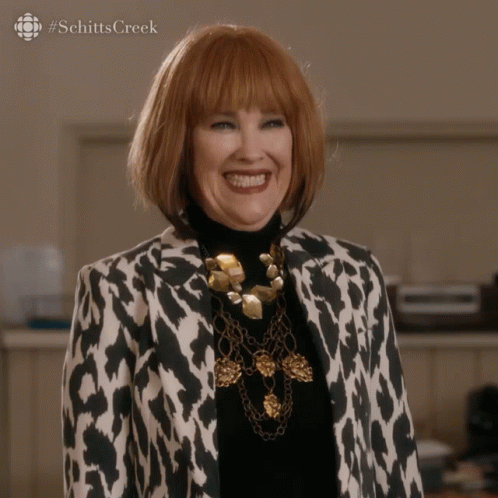 A Woman Wearing A Leopard Print Jacket And A Gold Necklace Smiles For The Camera GIF