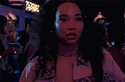 A Woman Wearing A Leopard Print Jacket And A Necklace Is Standing In A Dark Room . GIF