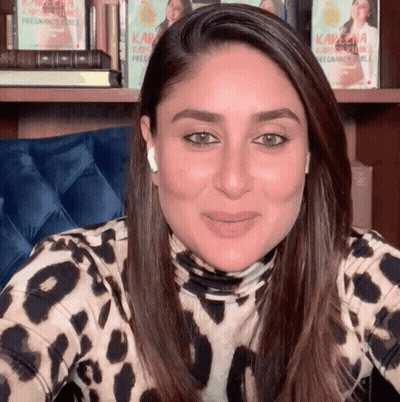 A Woman Wearing A Leopard Print Shirt Is Smiling In Front Of A Bookshelf With Kareena Kapoor Books GIF
