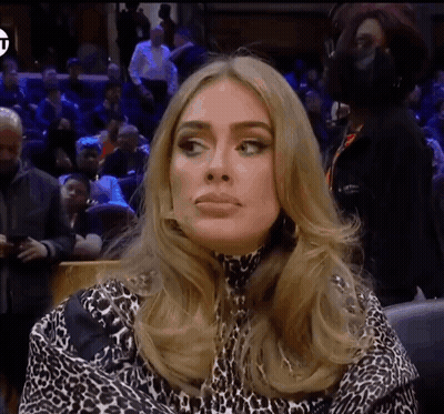 A Woman Wearing A Leopard Print Top Is Sitting In Front Of A Crowd GIF
