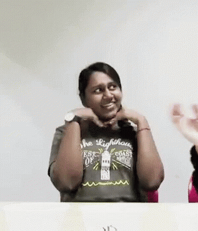 A Woman Wearing A Lighthouse T-Shirt Is Sitting At A Table With Her Hands On Her Face . GIF